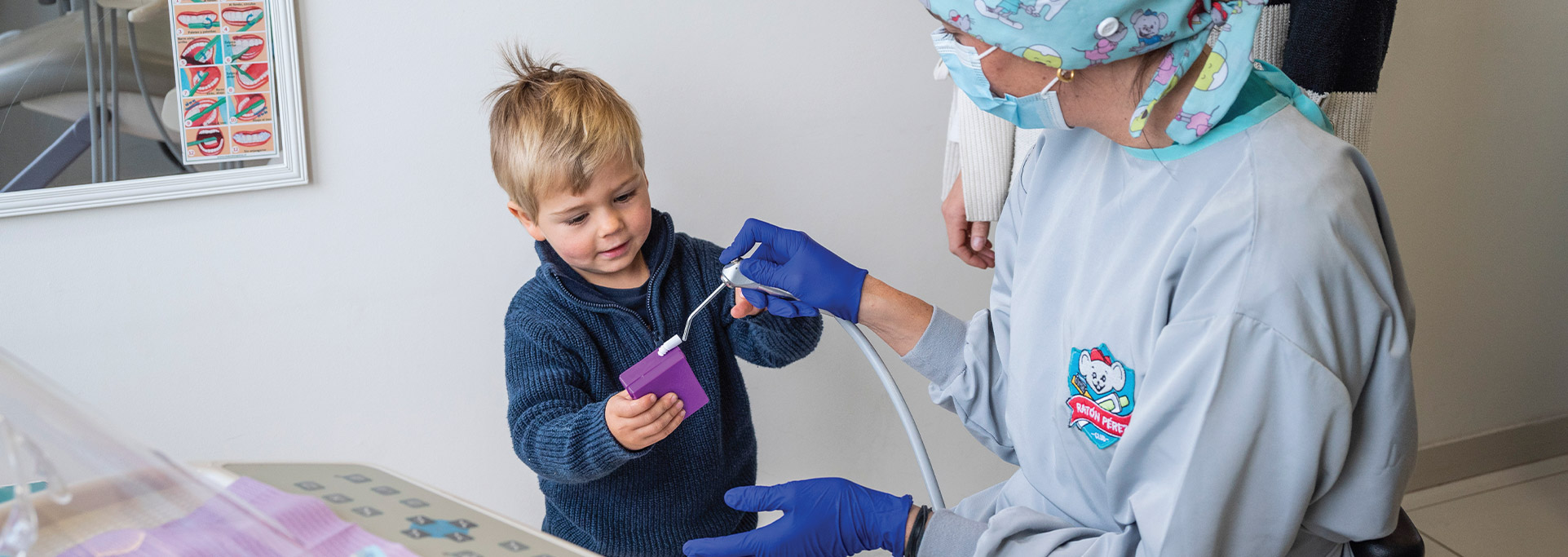 Niño rubio interactúa feliz con el equipo dental, guiado por la odontopediatra de Club Ratón Pérez. Ideal para primera visita y odontología sin miedo.